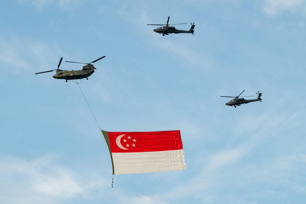 Three military helicopters flying high in clear blue skies carrying the Singapore flag, showcasing a powerful aerial display.